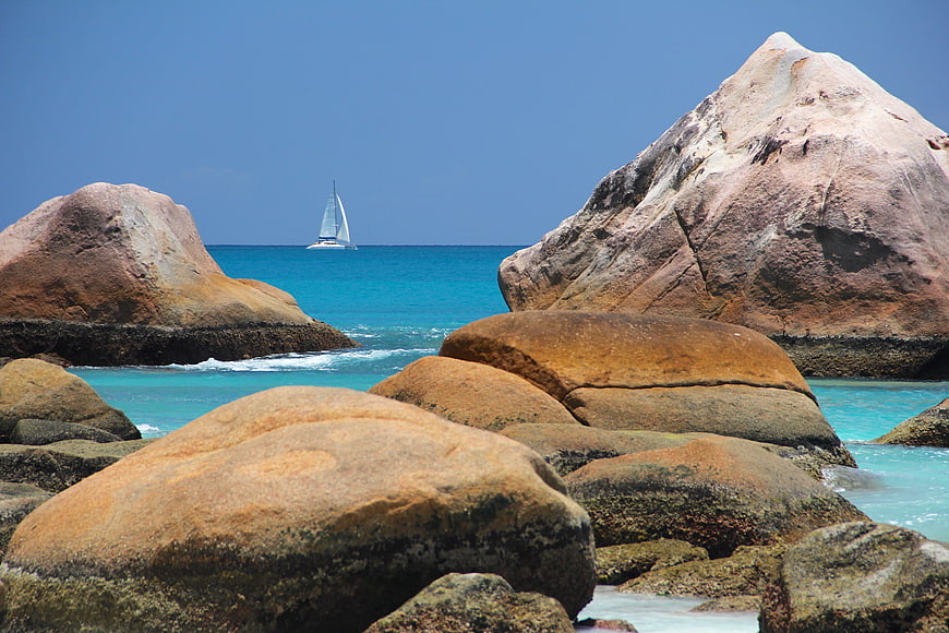 Sailboat on turquoise sea between large granite boulders