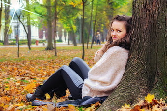 Young woman in beige sweater sitting on autumn leaves in a park