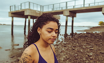 Portrait of woman with tattoos standing by pier on cloudy day
