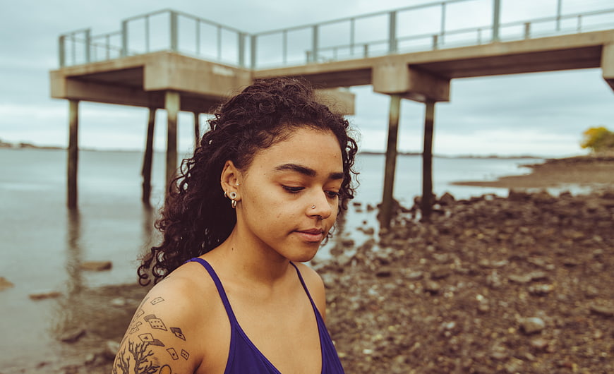 Portrait of woman with tattoos standing by pier on cloudy day