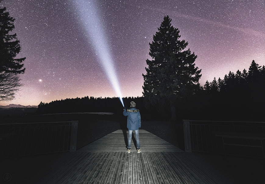 Person Stargazing with Flashlight on Wooden Deck at Night