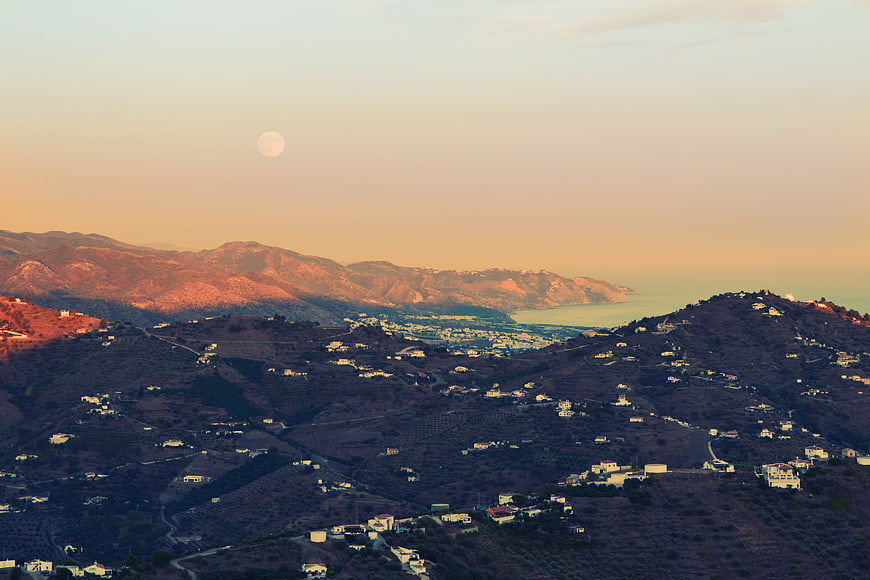 Scenic coastal mountain landscape with moon and village at sunset