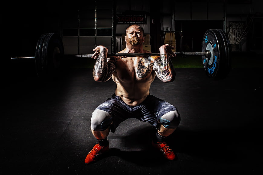 Tattooed Man Performing Heavy Barbell Squat in Dark Gym