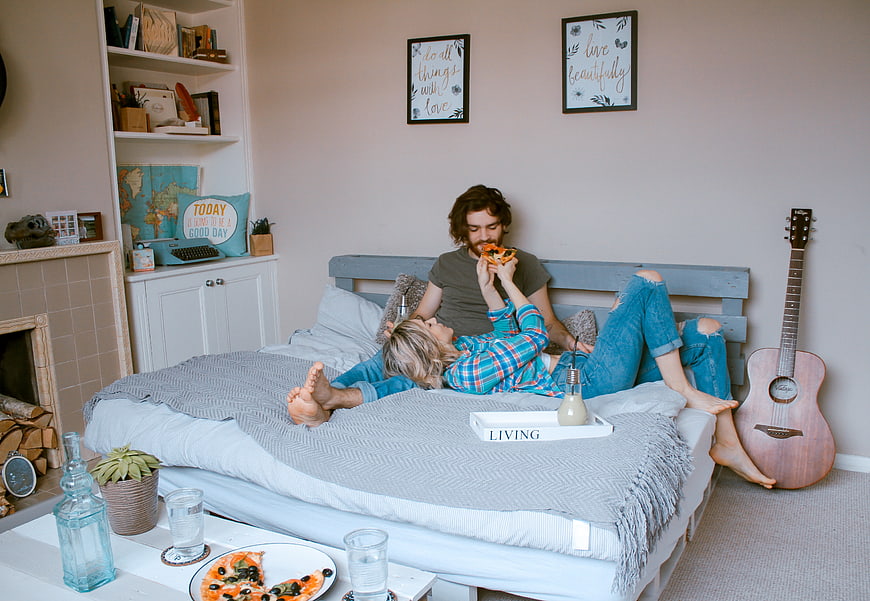 Couple eating pizza on bed in cozy living room
