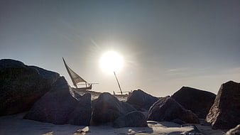 Silhouetted traditional sailboats on rocky beach at sunset