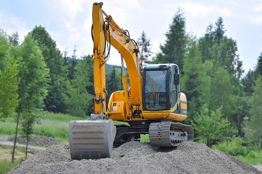 Yellow Excavator on Gravel Pile in Forest