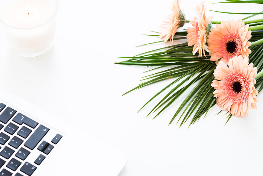 Minimalist workspace with laptop, candle, and pink gerbera flowers