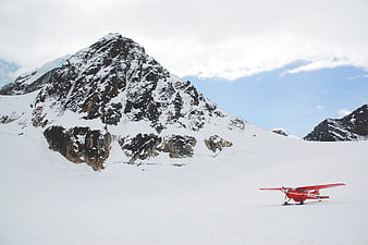 Red ski plane on snowy glacier with mountain peak