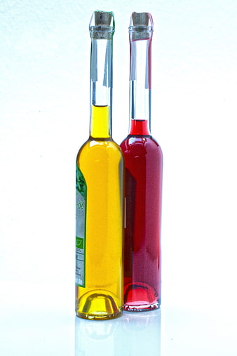 Two glass bottles containing yellow olive oil and red raspberry vinegar