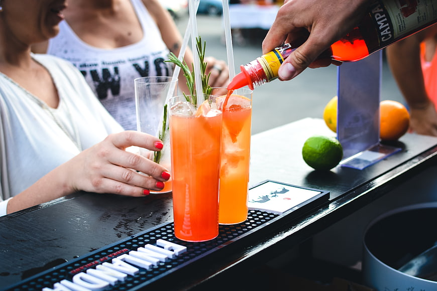 Bartender pouring red syrup into orange cocktails at outdoor bar