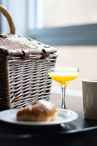 Wicker picnic basket with orange juice and croissant on table