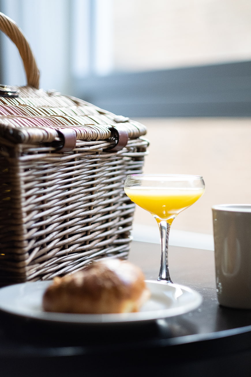 Wicker picnic basket with orange juice and croissant on table