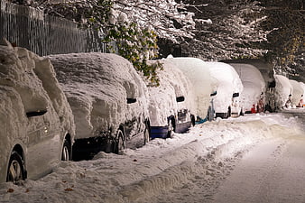 Snow-covered cars parked on a city street at night