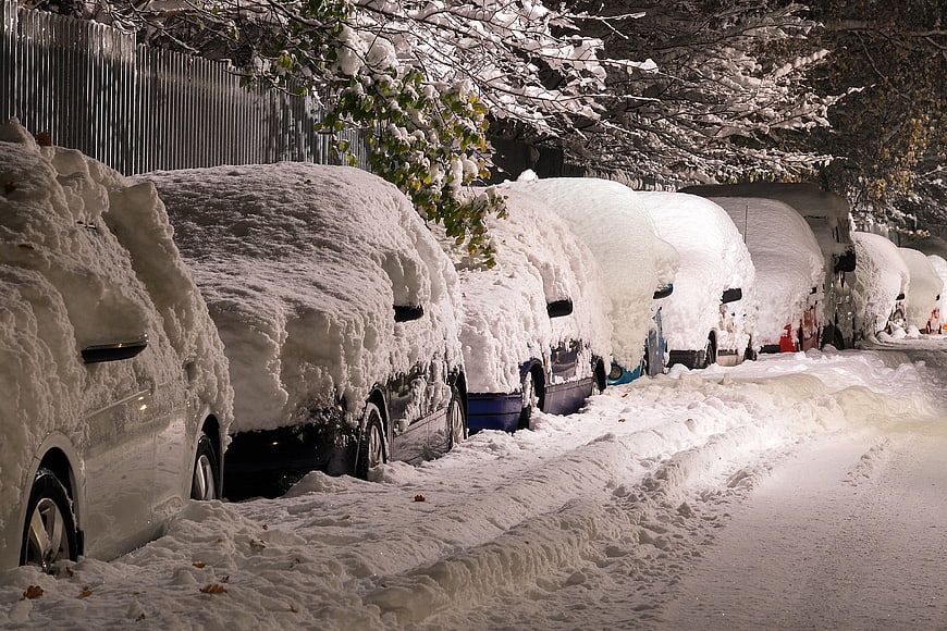 Snow-covered cars parked on a city street at night