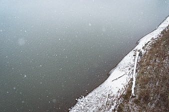 Aerial View of Snowy Lake Shore with Falling Snowflakes