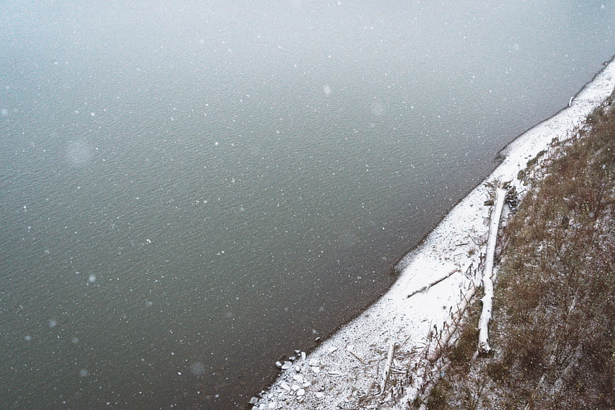 Aerial View of Snowy Lake Shore with Falling Snowflakes