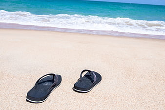 Black Flip Flops on Sandy Beach with Ocean Waves