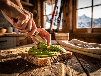 Hands Slicing Avocado on Toast in Rustic Cabin