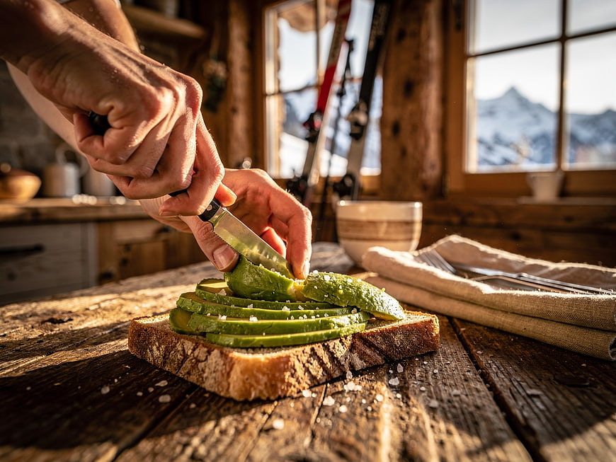 Hands Slicing Avocado on Toast in Rustic Cabin