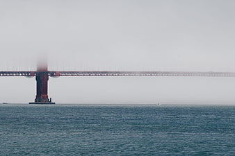 Foggy red bridge tower over calm blue ocean water