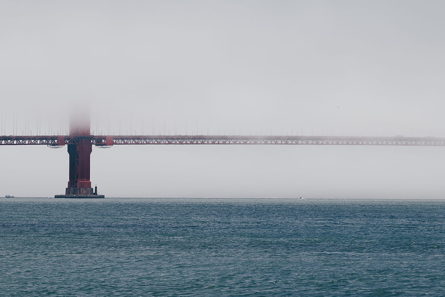 Foggy red bridge tower over calm blue ocean water
