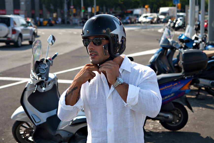 Man in White Shirt Adjusting Motorcycle Helmet on Street