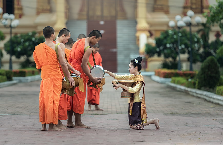 Buddhist monks receiving alms from kneeling woman in traditional dress