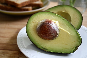 Fresh halved avocado with pit on white plate with toast in background