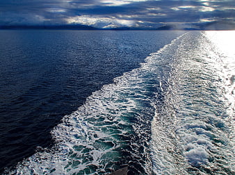 Boat wake trail on deep blue ocean with distant mountains
