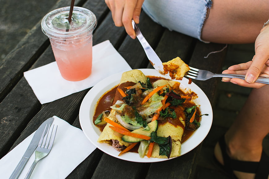 Overhead view of hands eating enchiladas and pink drink outdoors
