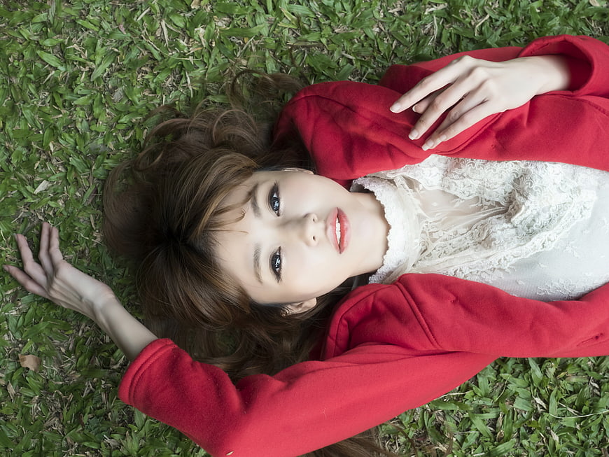 Young Asian Woman Lying on Grass in Red Jacket
