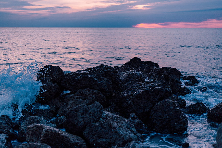 Dramatic Sunset Over Rocky Coastline with Crashing Waves