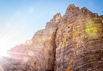 Rock climbers ascending steep mountain face with sun flare