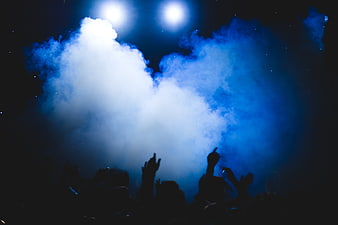 Silhouettes of crowd hands raised at concert with blue smoke