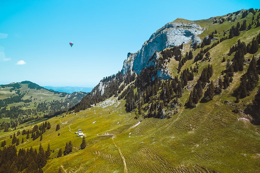 Aerial view of green mountain slope with paraglider and rocky cliff