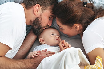 Happy Parents Kissing Newborn Baby on Bed