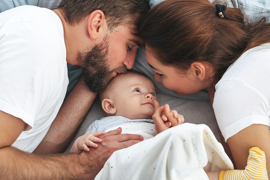 Happy Parents Kissing Newborn Baby on Bed