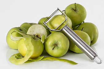 Fresh green apples with peeler and peels on white background