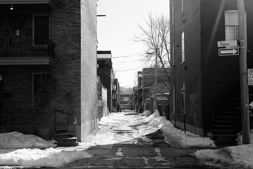 Black and white photo of snowy urban alleyway between brick buildings