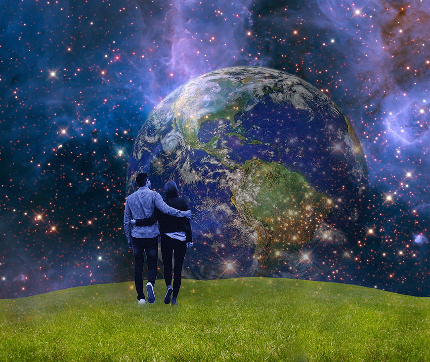 Couple standing on grass hill looking at giant Earth in space