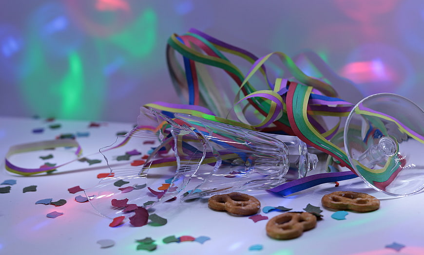 Broken champagne glass with confetti and pretzels on a white table