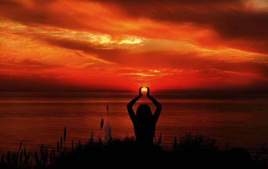 Silhouette of Woman Holding Sun Over Ocean at Sunset
