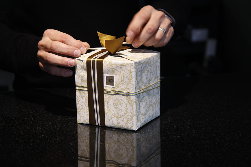 Hands tying gold ribbon on elegant gift box