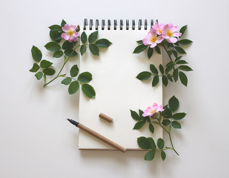Flat lay of notebook with pink wild roses and pen