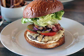 Gourmet burger with bacon, cheese, and lettuce on a white plate