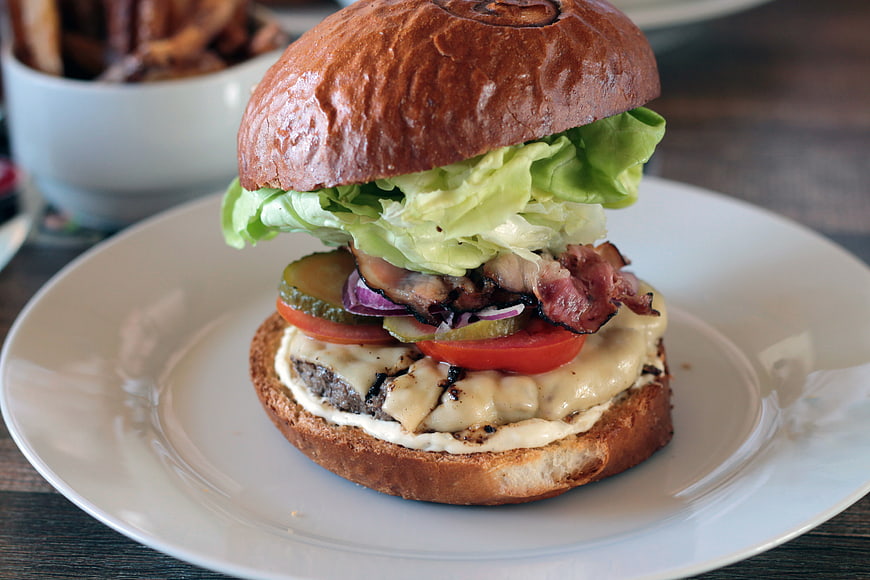 Gourmet burger with bacon, cheese, and lettuce on a white plate