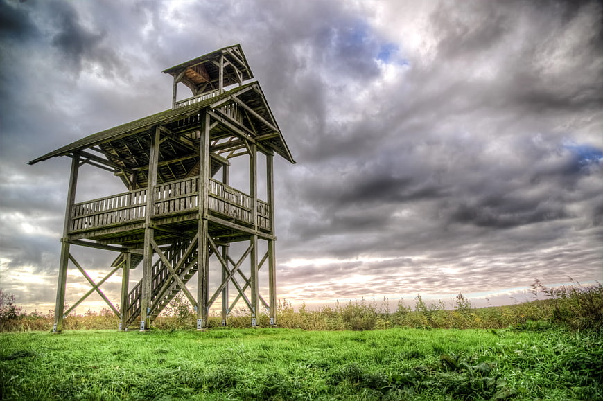 Wooden Observation Tower in Green Field Under Dramatic Clouds