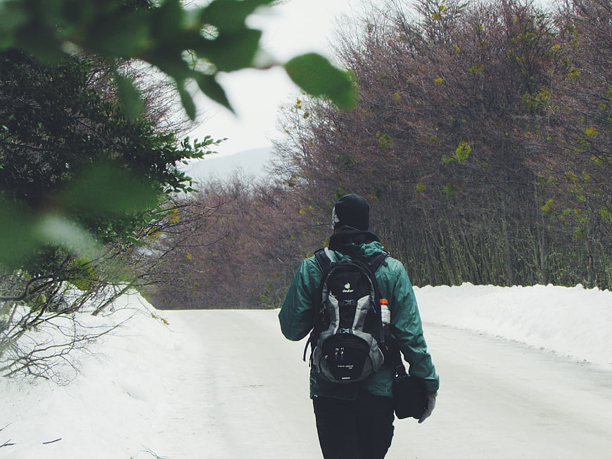 Hiker with backpack walking on snowy winter road