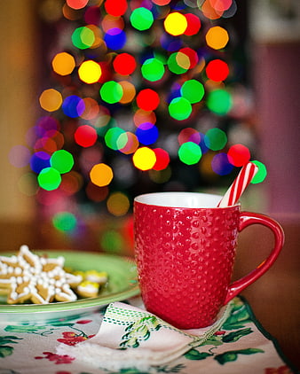 Red mug with candy cane and gingerbread cookies near Christmas tree