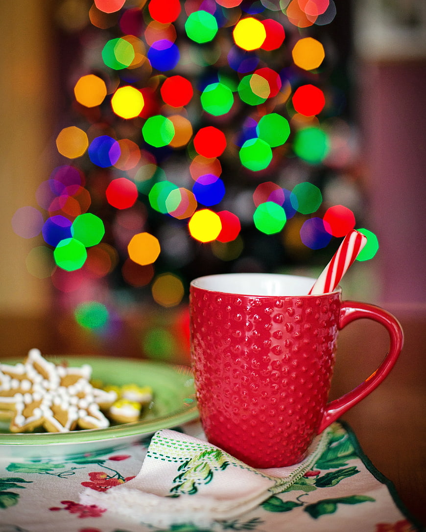 Red mug with candy cane and gingerbread cookies near Christmas tree
